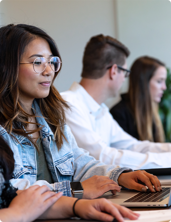 Woman with glasses using a laptop in a group.