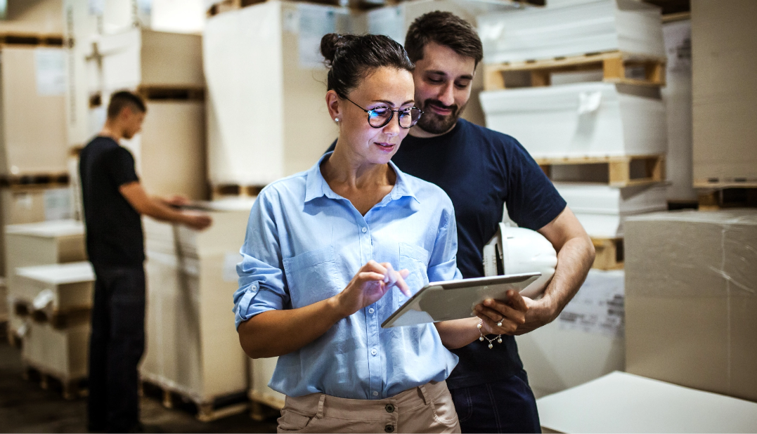 Man and woman in warehouse looking at tablet.