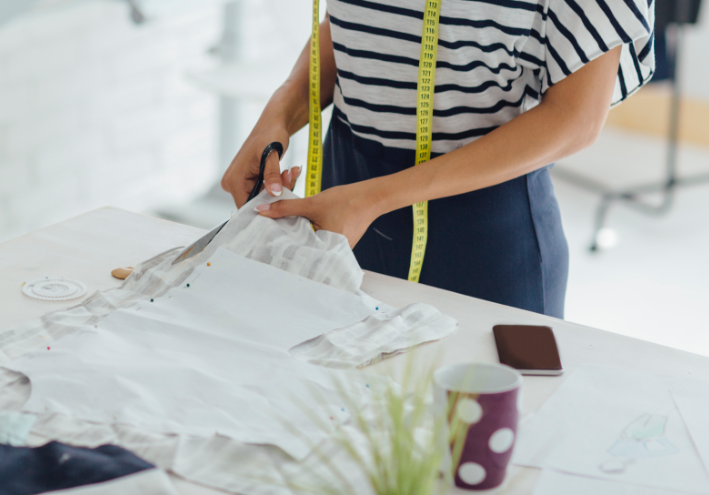 Woman with measuring tape cutting fabric.