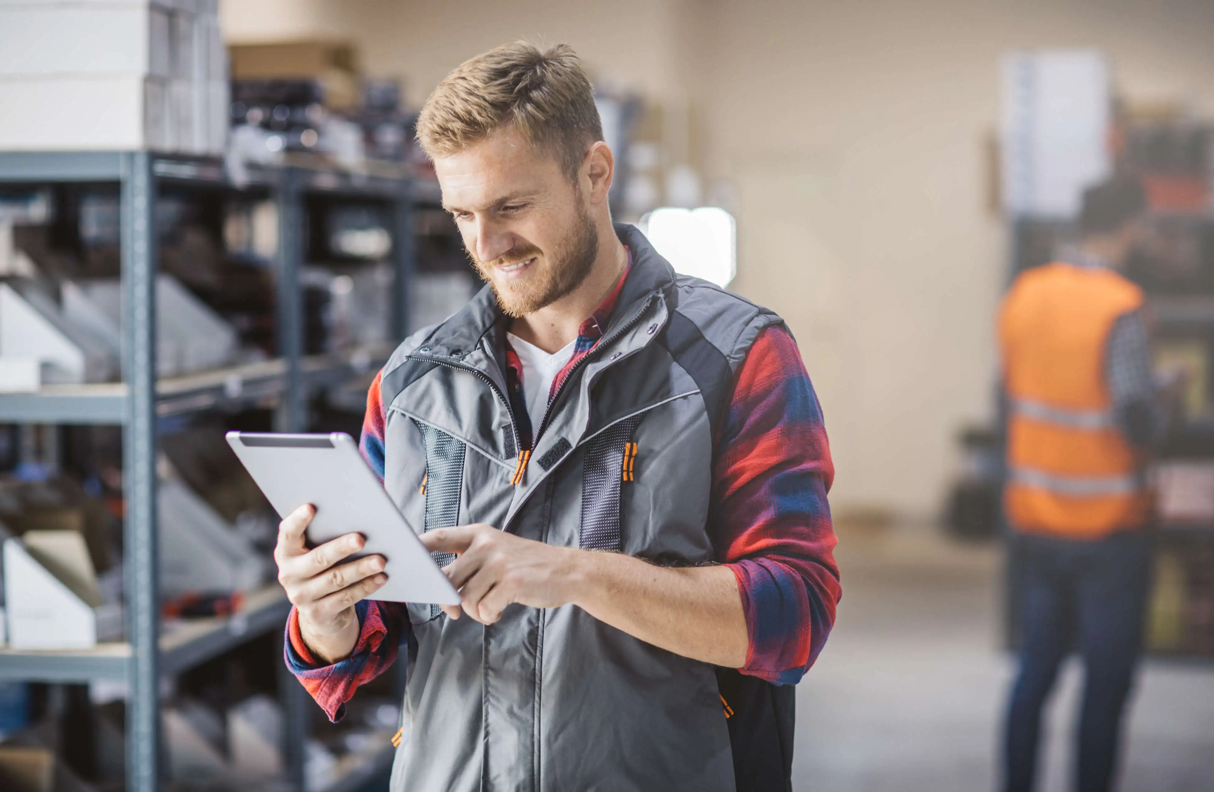 A man in a warehouse looking at a tablet and smiling.