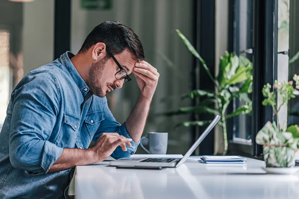 A man looking at a laptop frustratingly.